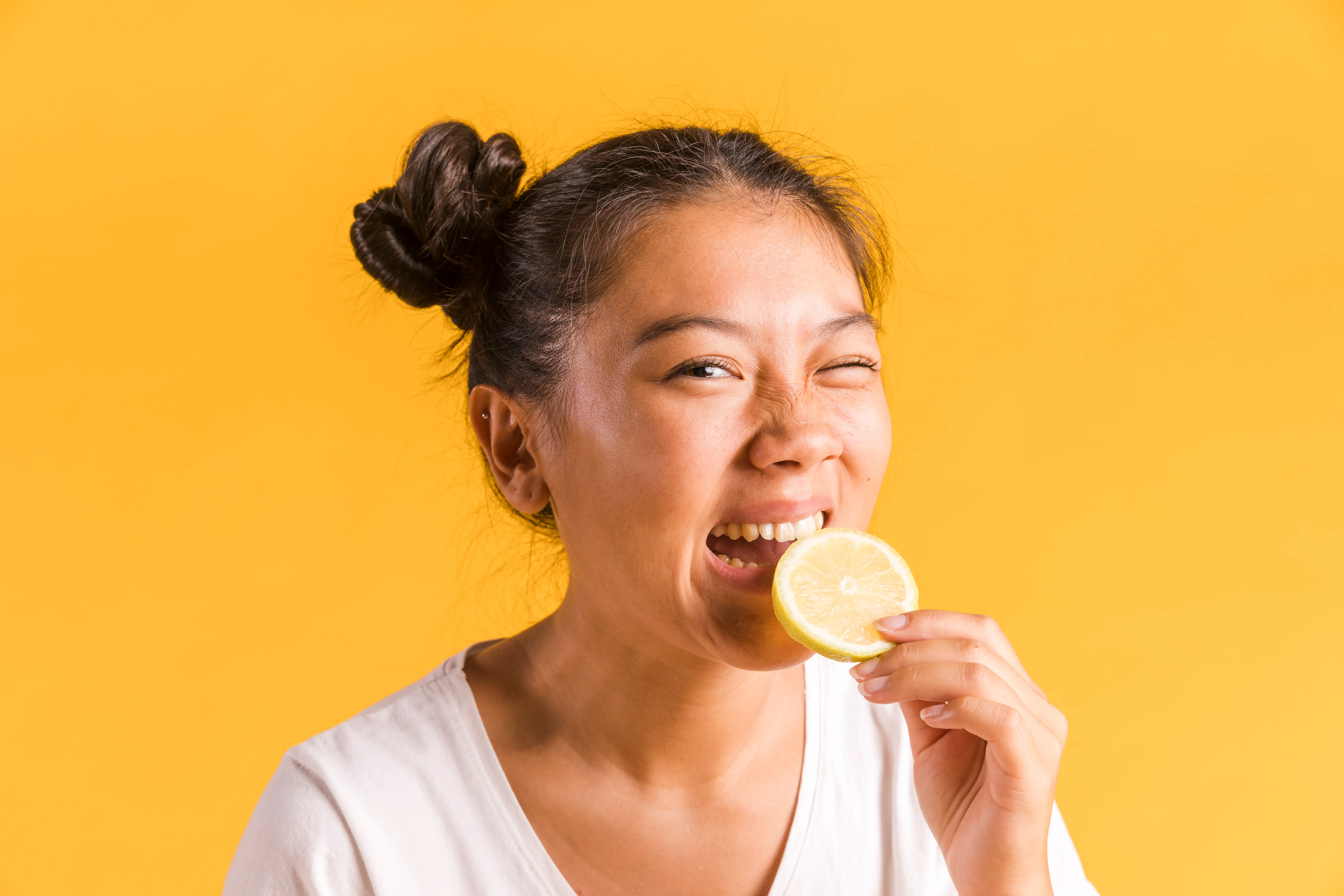 Woman experiencing sharp tooth pain while biting a lemon due to acid sensitivity